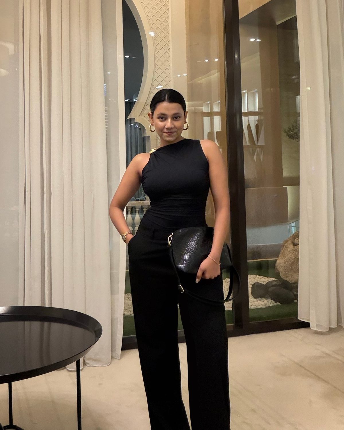 Sneha David in a black one-shoulder top and wide-leg trousers
